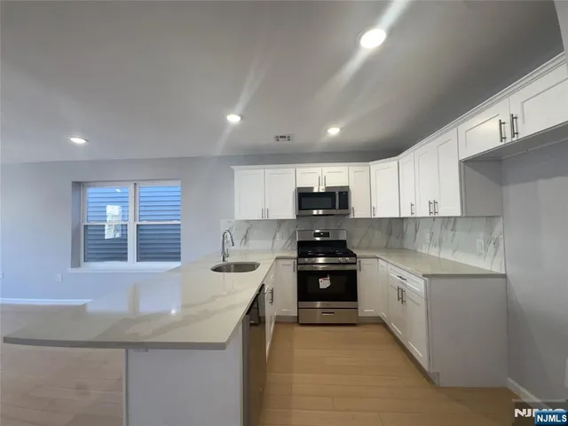 an empty room with wooden floor kitchen view and windows