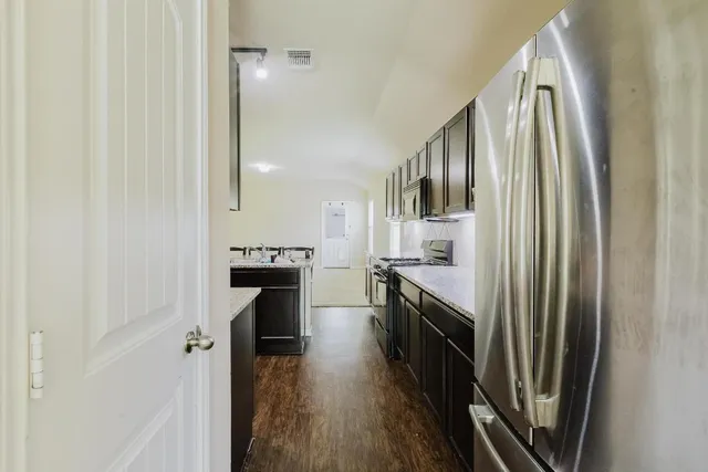 a kitchen with stainless steel appliances granite countertop a refrigerator a stove and a sink with wooden floor