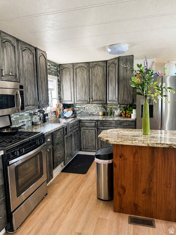 33 Apollo Way Sandy, UT 84070 - Photo 7 of 9 Kitchen with stainless steel appliances, a textured ceiling, light wood-style flooring, decorative backsplash, and dark wood finish cabinetry