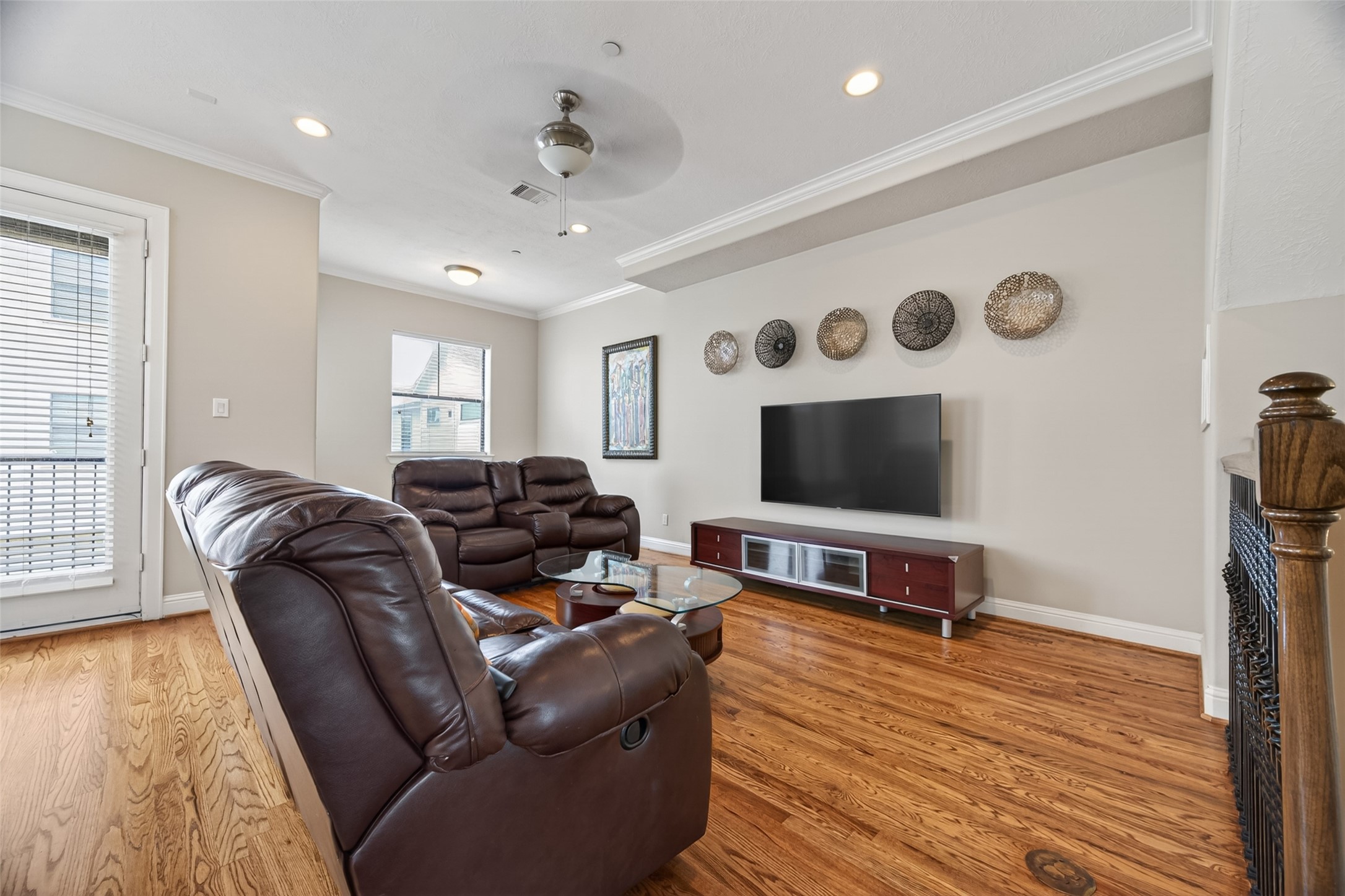2611 Riverside Drive, Unit C Houston, TX 77004 - Photo 26 of 50 Bright living room with hardwood floors, featuring comfortable leather seating, a wall-mounted TV, and decorative wall art. Large windows and a glass door provide natural light, creating an inviting space.