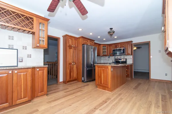 a kitchen with stainless steel appliances kitchen island granite countertop a refrigerator a oven a sink with wooden cabinets and wooden floor