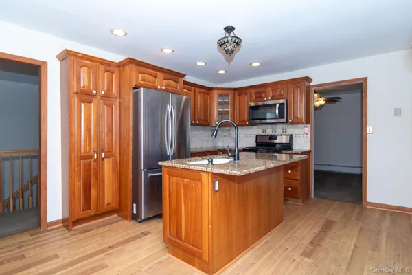 a large kitchen with stainless steel appliances granite countertop a refrigerator a sink and a stove with wooden floor