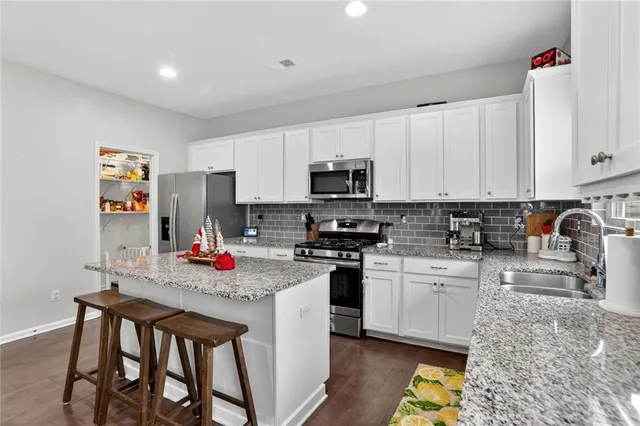 a kitchen with stainless steel appliances granite countertop a stove top oven a sink dishwasher and white cabinets with wooden floor