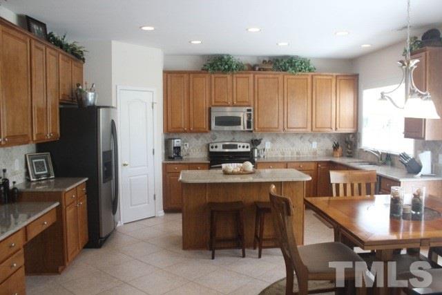 7729 Silver View Lane Raleigh, NC 27613 - Photo 7 of 25 a kitchen with kitchen island granite countertop a stove top oven a sink a refrigerator and chairs