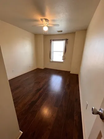 an empty room with wooden floor fan and windows