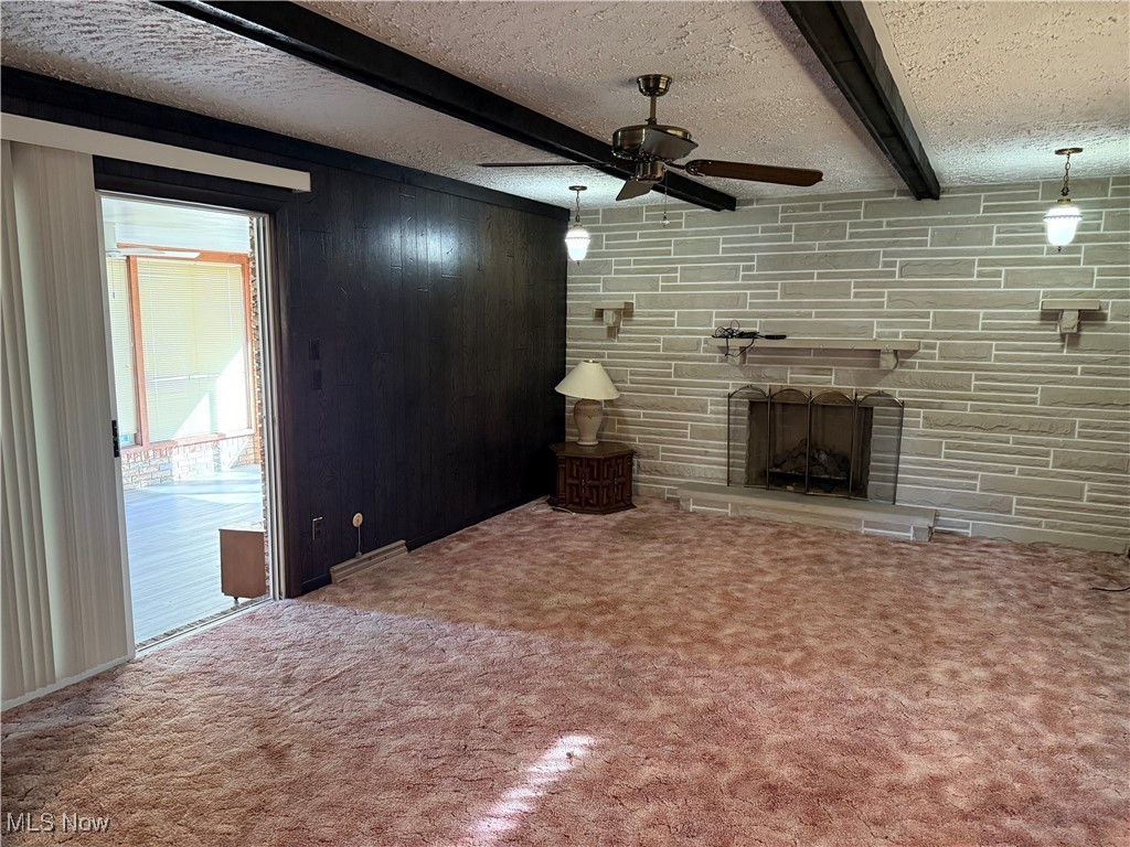 683 Robinson Road Campbell, OH 44405 - Photo 8 of 23 Unfurnished living room with beam ceiling, a textured ceiling, carpet, a fireplace, and wood walls