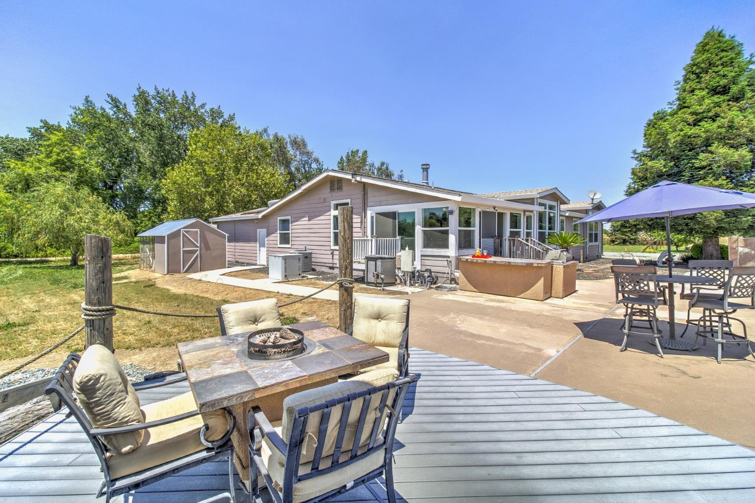 12390 Hobday Road Wilton, CA 95693 - Photo 57 of 92 a view of a patio with couches table and chairs under an umbrella with wooden floor and fence