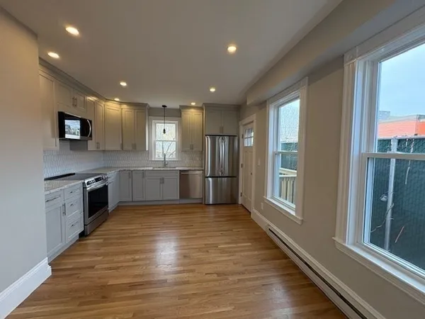 a large kitchen with stainless steel appliances granite countertop a large counter top a oven and a sink with wooden floor