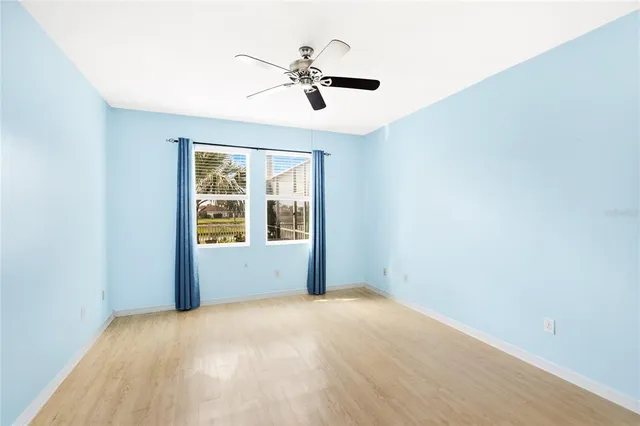 an empty room with wooden floor ceiling fan and windows