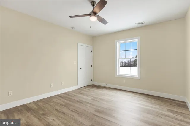 an empty room with wooden floor ceiling fan and windows