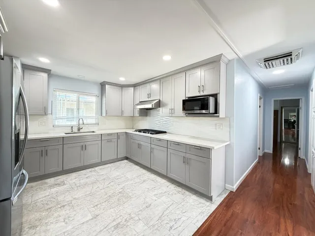 a kitchen with stainless steel appliances granite countertop a refrigerator oven a sink dishwasher and white cabinets with wooden floor