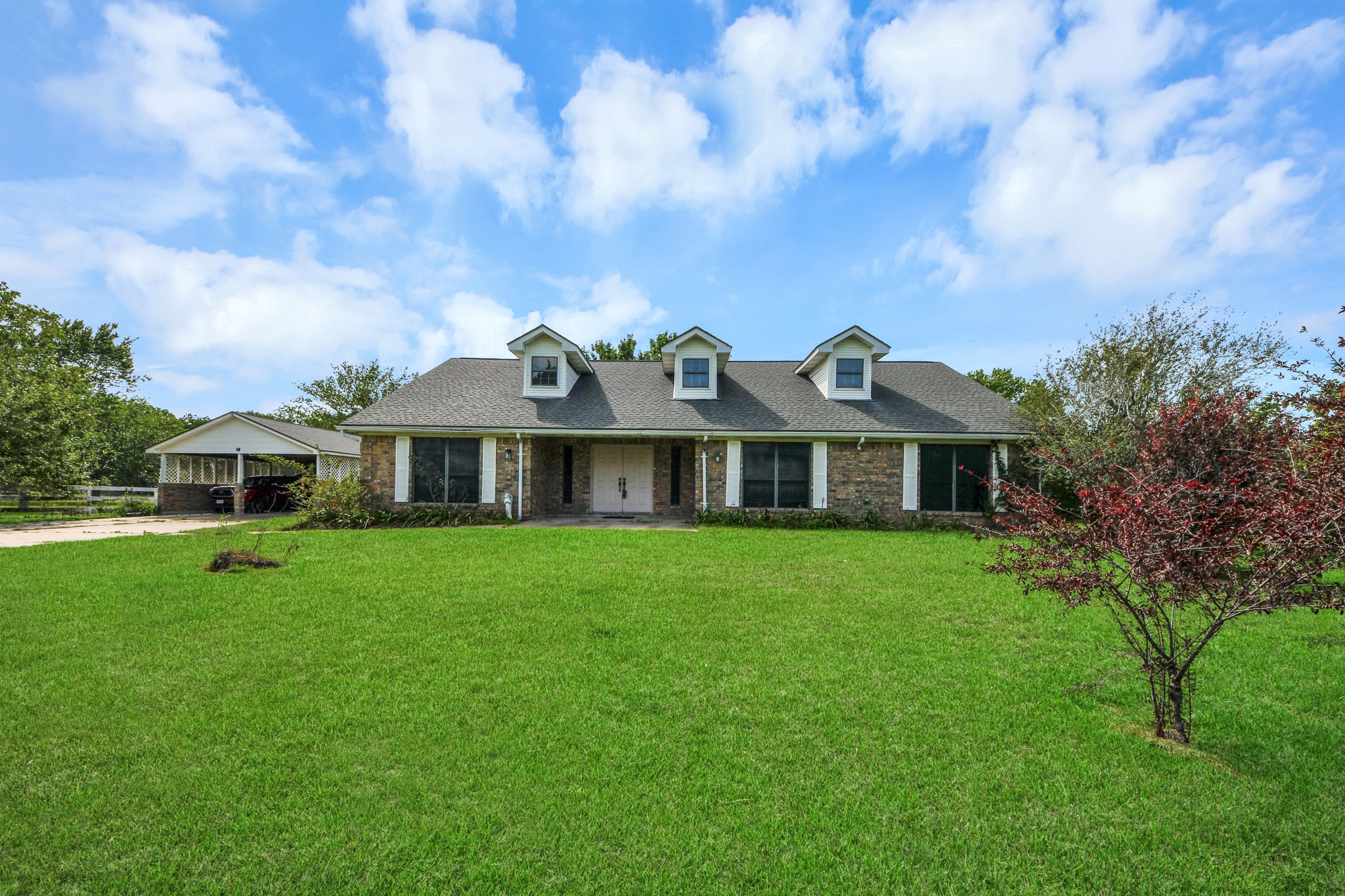 12746 Roy Road Pearland, TX 77581 - Photo 3 of 47 Charming single-story brick home with a large front lawn, featuring three dormer windows on the roof. It includes a detached garage and is surrounded by greenery, offering a peaceful suburban feel.