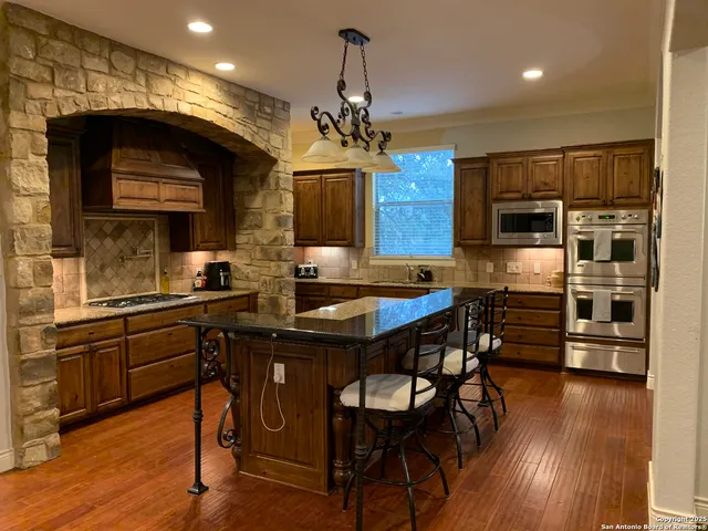 a kitchen with stainless steel appliances granite countertop a stove a refrigerator a sink dishwasher a dining table and chairs with wooden floor