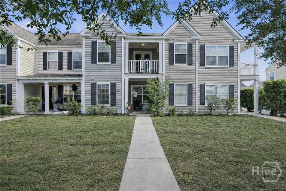 Two-story townhouse-style condo with covered front porch, neutral siding, black shutters, and private front entry.