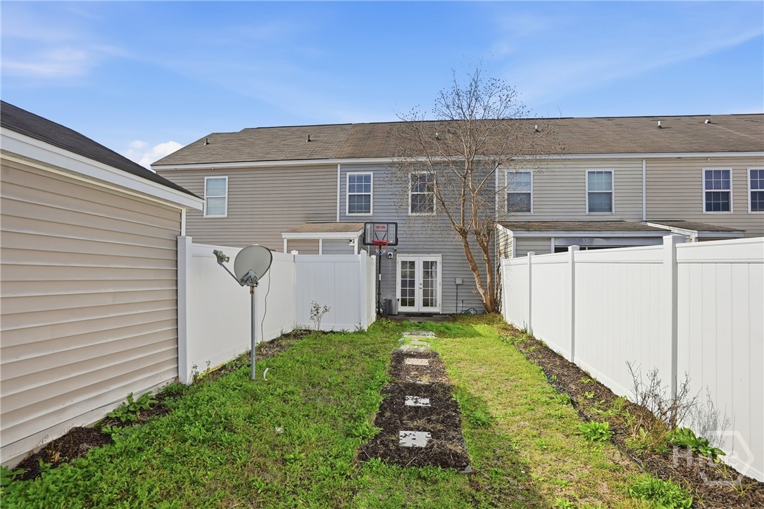 61 Timber Crest Court Savannah, GA 31407 - Photo 25 of 29 Private fenced backyard with grass lawn, rear entry doors, and paved walkway behind a two-story townhouse