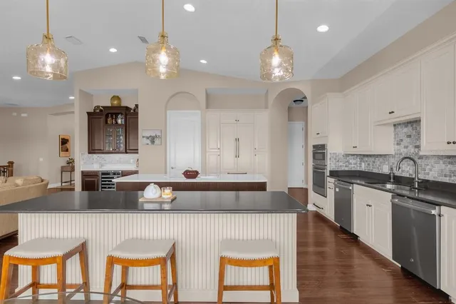 a large kitchen with a large island in the center a sink dishwasher a dining table and chairs with wooden floor