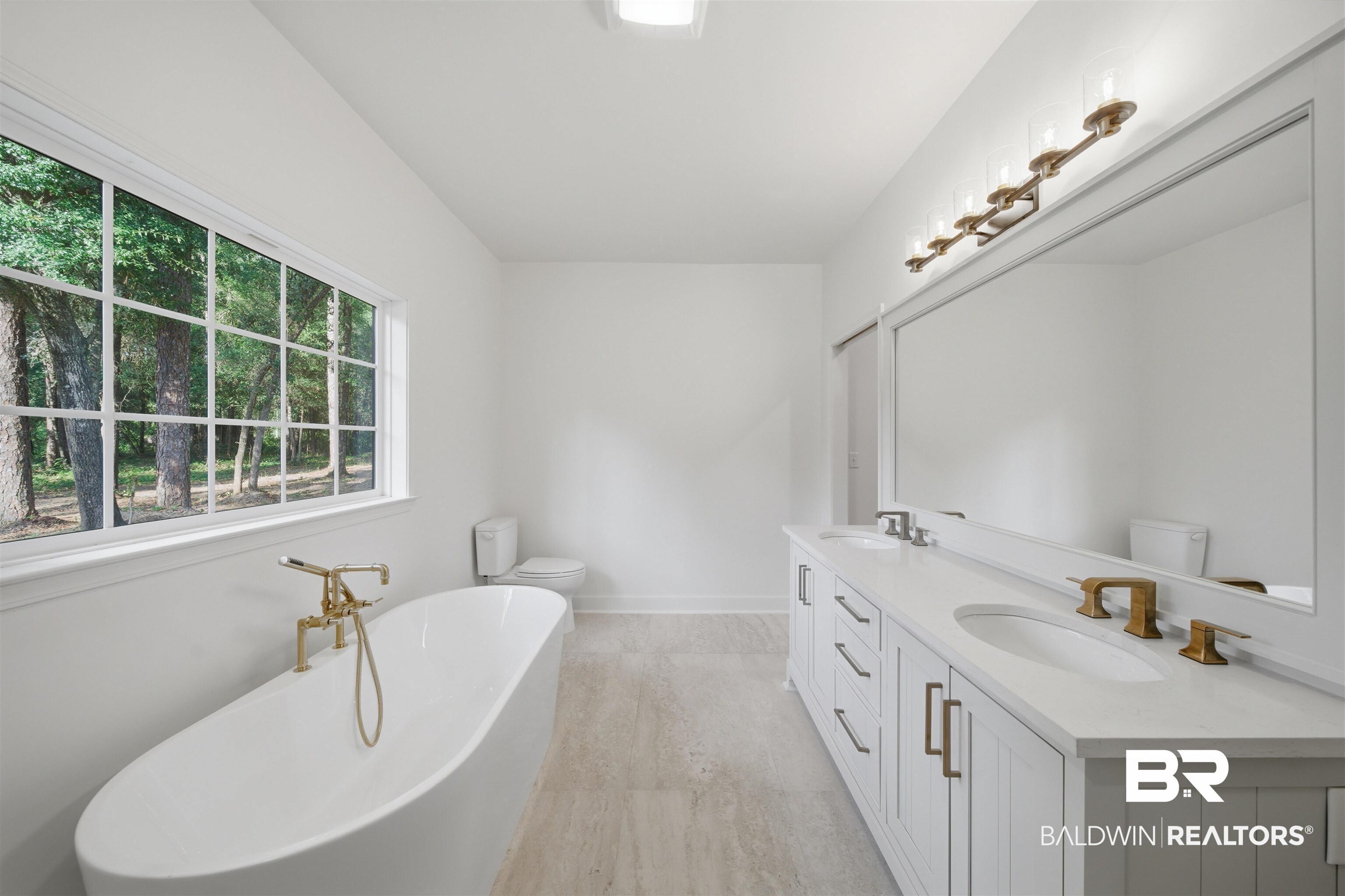 14128 Jackson Lane Foley, AL 36535 - Photo 21 of 36 Contemporary bathroom featuring a freestanding soaking tub with brass fixtures, a dual-sink vanity with white cabinetry and stone countertops, and a wide window with grid detailing