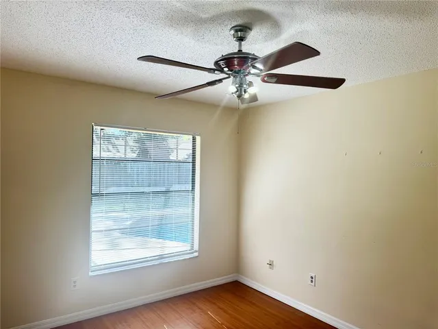 an empty room with wooden floor fan and windows