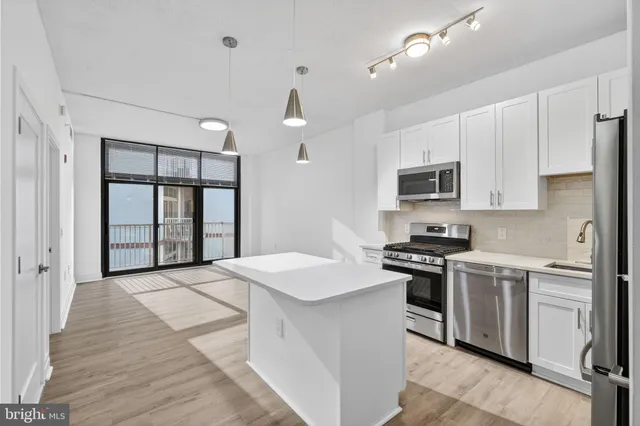 a kitchen with stainless steel appliances a stove a sink dishwasher a refrigerator white cabinets and wooden floor