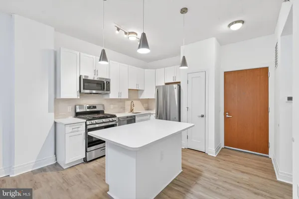 a kitchen with stainless steel appliances a stove a sink dishwasher a refrigerator white cabinets and wooden floor