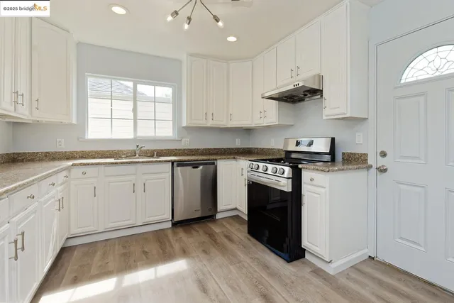 a kitchen with stainless steel appliances granite countertop a stove a sink and white cabinets