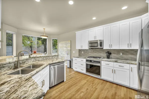 a kitchen with stainless steel appliances granite countertop a stove top oven a sink dishwasher a refrigerator and white cabinets with wooden floor