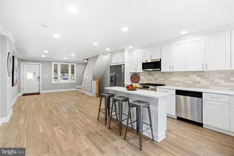 a kitchen with stainless steel appliances granite countertop a stove a sink a refrigerator and white cabinets with wooden floor