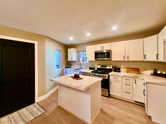 a kitchen with stainless steel appliances granite countertop a stove top oven a refrigerator a sink and dishwasher with wooden floor