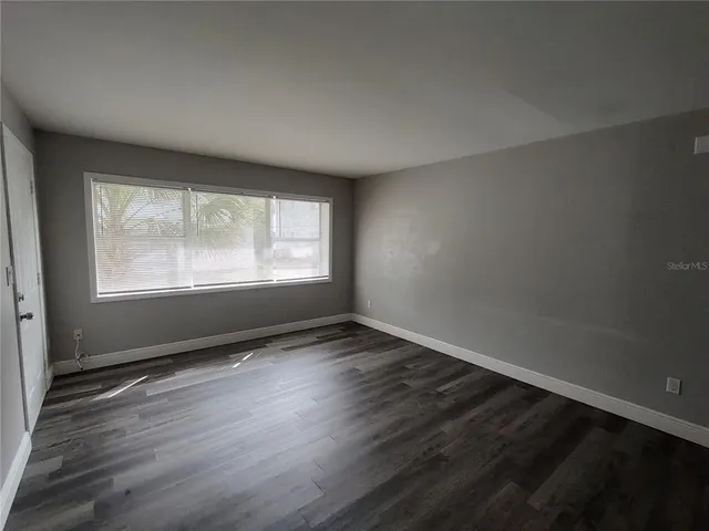 a view of an empty room with wooden floor and a window