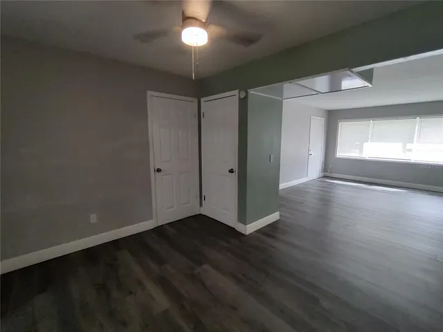an empty room with wooden floor chandelier fan and windows