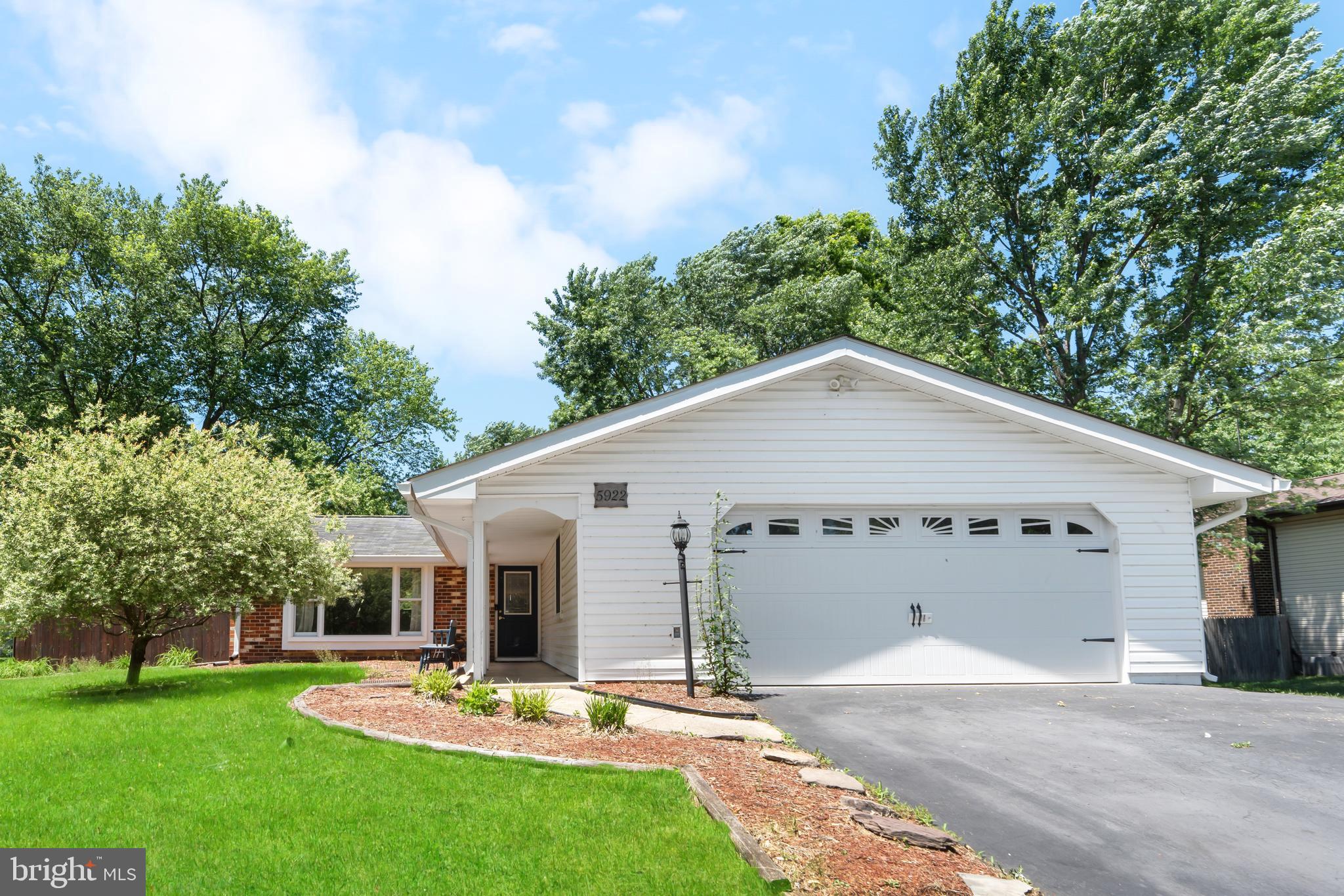 a view of a white house with a yard potted plants and large tree