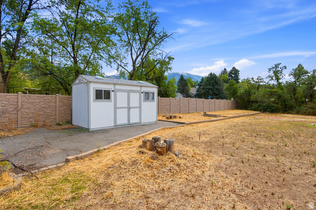 2315 Creek Road Sandy, UT 84093 - Photo 30 of 32 Expansive outdoor space featuring a detached storage shed with dual doors and windows, a paved pathway, and a perimeter fence