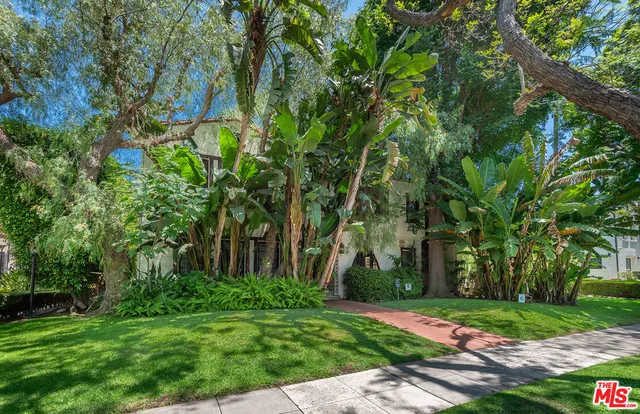 a view of a white house with a big yard plants and large trees