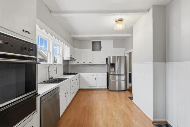 a kitchen with stainless steel appliances a refrigerator a sink and white cabinets
