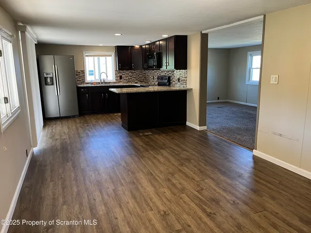 a kitchen with stainless steel appliances granite countertop a refrigerator a sink dishwasher a stove and white countertops with wooden floor