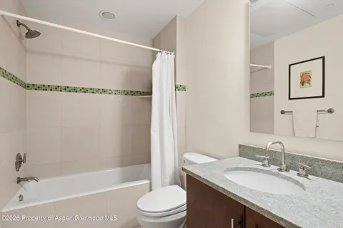 a bathroom with a granite countertop bathtub shower sink vanity mirror and toilet