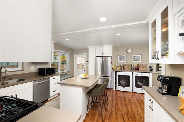 a kitchen with stainless steel appliances a stove top oven a sink a refrigerator white cabinets and wooden floor