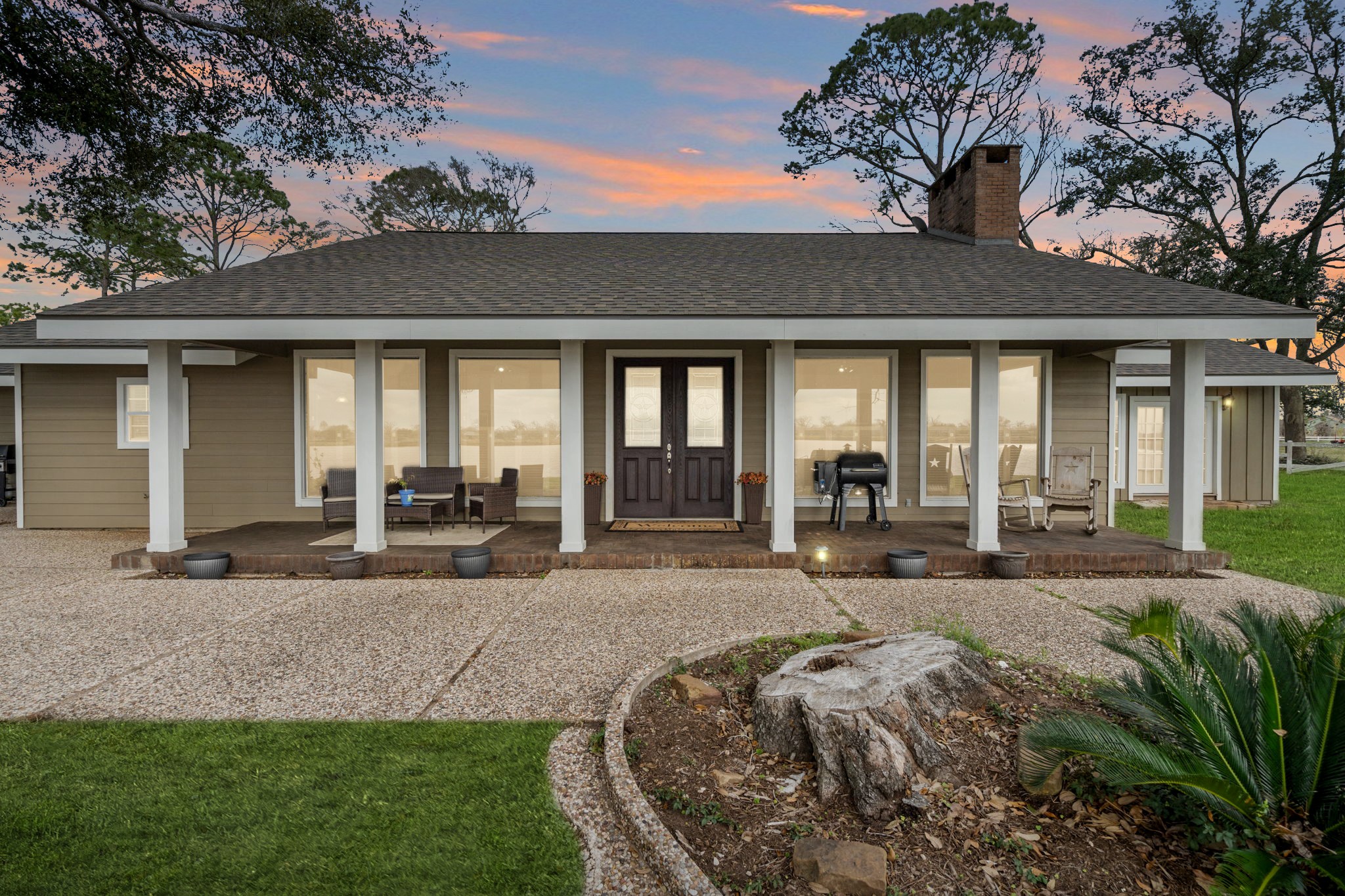 This classic ranch-style home presents a warm, welcoming façade anchored by a wide, covered front porch that stretches across the front of the house. Sturdy columns, brick porch flooring, and generous seating areas create an inviting place to relax and take in the surrounding views.