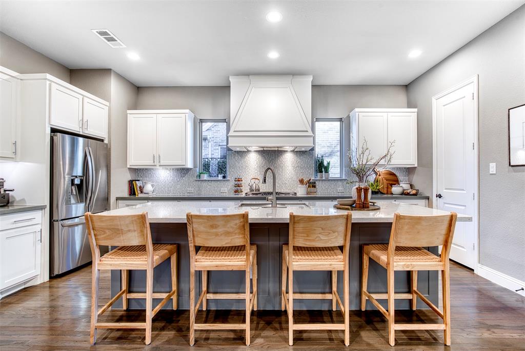 5904 Rutland Road McKinney, TX 75070 - Photo 10 of 40 Two tone kitchen with stainless steel fridge with ice dispenser, hardwood floors, an island with sink, dual tone cabinets, mosiac glass blacksplash and light stone countertops