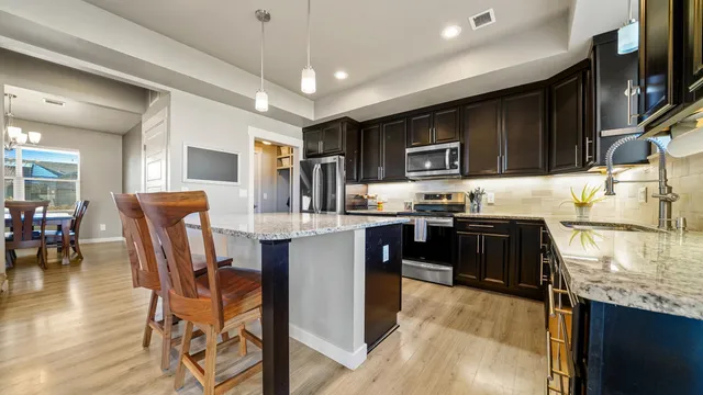 a kitchen with stainless steel appliances granite countertop a stove top oven a sink dishwasher a dining table and chairs with wooden floor