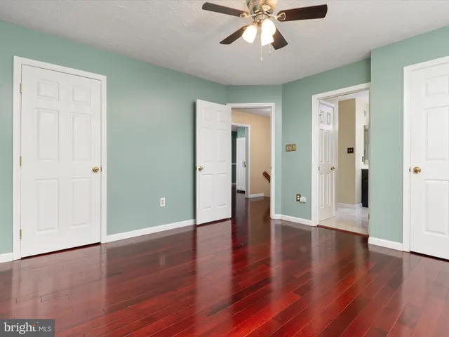 a view of an empty room with wooden floor and a ceiling fan