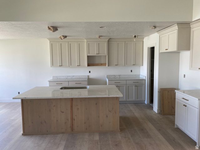 4676 West 75 North, Unit 401 West Point, UT 84015 - Photo 3 of 17 Spacious kitchen featuring a large central island with an undermount sink, light-toned wood-finish flooring, white perimeter cabinetry, and light-toned countertops throughout
