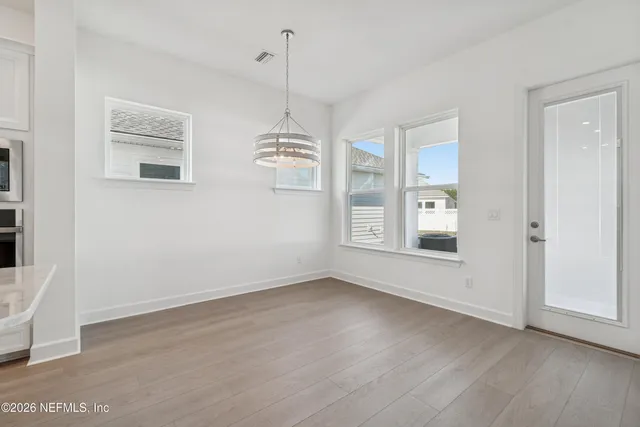 an empty room with wooden floor chandelier and windows