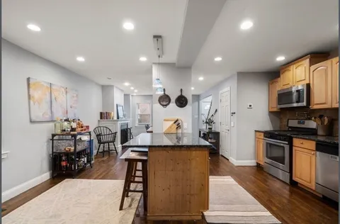 a large living room with stainless steel appliances kitchen island granite countertop a large kitchen island a stove a sink a dining table and chairs with wooden floor