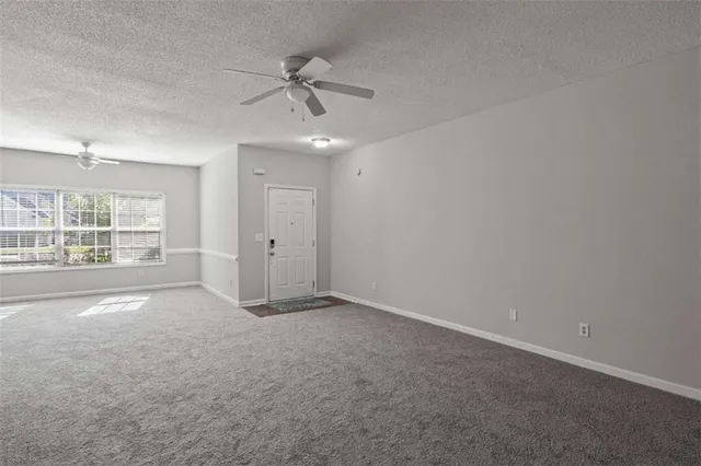 an empty room with chandelier fan and windows