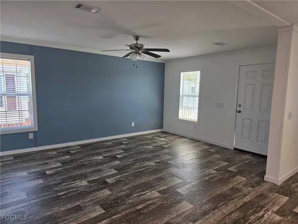 an empty room with wooden floor chandelier fan and windows