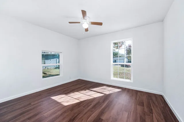 an empty room with wooden floor chandelier fan and windows
