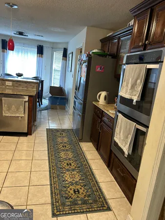 a living room with stainless steel appliances furniture a rug and a kitchen view