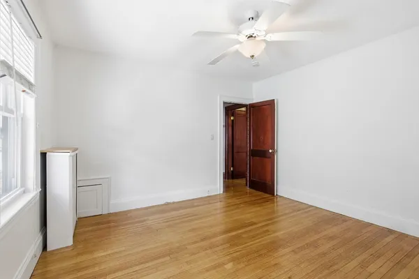 a view of an empty room with wooden floor and a ceiling fan