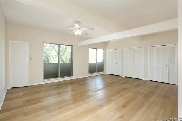 an empty room with wooden floor fan and windows
